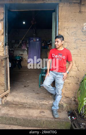 Ahuachapán, El Salvador - November 04 2022: A Salvadoran Young Man Stands Happily at the Enter of a Rustic Adobe House Stock Photo