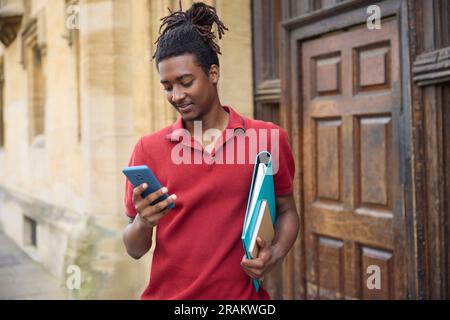 Male Student Checking Messages Or Social Media On Mobile Phone Outside University Building In Oxford UK Stock Photo
