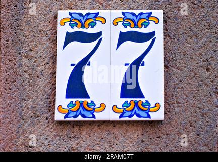 77, number seventy-seven, decorative tilework on gray surface. Stock Photo