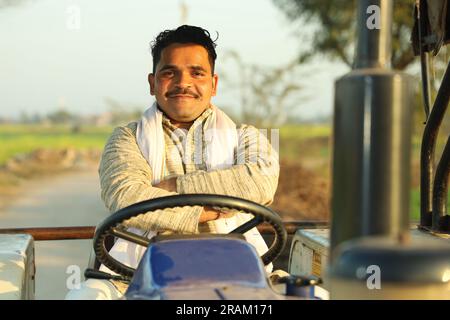 Young happy Indian farmer sitting on a tractor in a day time. Hard working rural farmer is ready for the day. Stock Photo