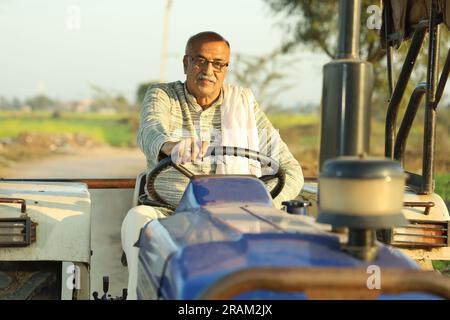 Happy hard working Indian farmer sitting on a tractor in a day time. Ready to start the day. Stock Photo