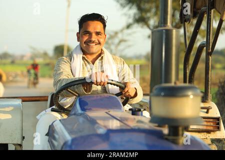 Happy hard working Indian farmer sitting on a tractor in a day time. Ready to start the day. Stock Photo