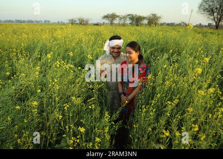 Happy Indian farmer couple standing in mustard field enjoying the agricultural profits. Money in hand. Happy to get benefitted by mustard crops. Stock Photo