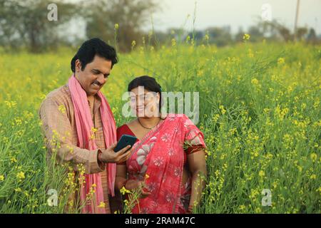 Young happy Indian farmer couple standing in mustard field holding ...