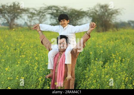 Young happy Indian farmer father standing in mustard field in day time ...