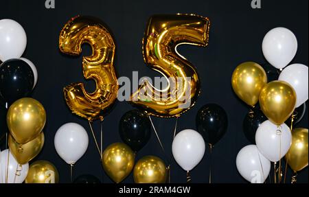 Celebrating 35 Years with Gold and Black Balloons. A festive birthday celebration with black and gold decorations, featuring a giant 35-year helium ba Stock Photo