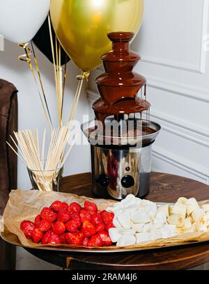 Chocolate fountain with strawberries and marshmallows on a wooden table Stock Photo