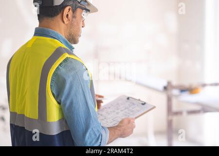 Focused engineer in protective helmet holds clipboard with renovation project in hands Stock Photo