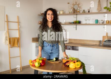 Happy arab woman cooking at home, smiling lady preparing healthy meal, looking and smiling at camera, kitchen interior Stock Photo