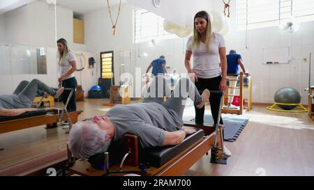Pilates Instructor Guiding Senior Woman on Machine, Old Age Workout Routine, spine health stretch Stock Photo