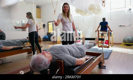 Pilates Instructor Guiding Senior Woman on Machine, Old Age Workout Routine, spine health stretch Stock Photo