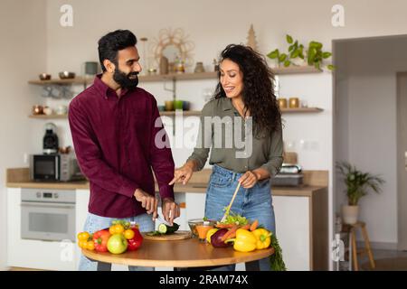 Cheerful young arab husband and wife enjoying cooking together, preparing healthy dinner and chatting, copy space Stock Photo
