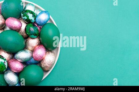 Mockup Easter food, treat. Colored chicken, quail eggs, chocolate eggs, sweets wrapped in bright foil on plate, top view. Flatly copy space Stock Photo