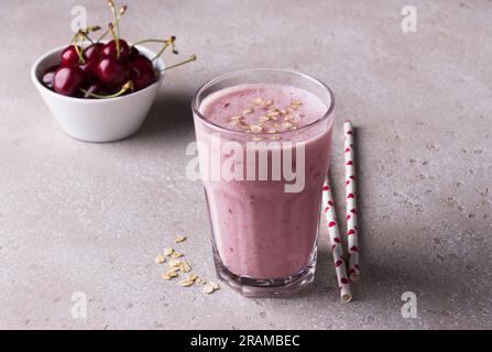 Milkshake with cherries, yogurt and oatmeal, drinking straws, bowl with fresh cherries on a beige textured background. Stock Photo