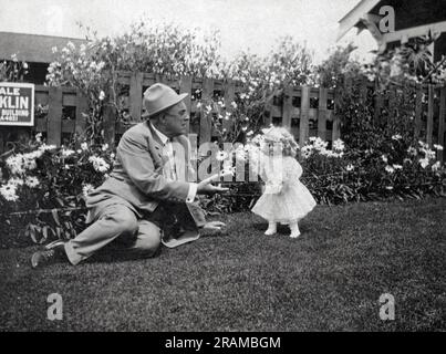 United States:  c. 1940 An older man in a suit sitting in a backyard talking to a doll. Stock Photo