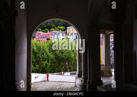 View of the pastel buildings in the historic town centre from the carriage entrance under the historic Sintra National Palace or in Palácio Nacional de Sintra in Sintra, Portugal. The Romanticist architectural and fairytale palaces draws tourists from around the world. Stock Photo