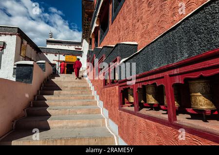 Young Buddhist monks walking on stairs along prayer wheels in Thiksey gompa Stock Photo