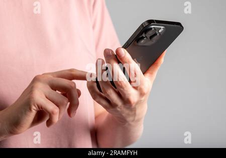 Berlin, Germany June 30 2023 Hand holding mobile phone, clicking tapping with finger on smartphone closeup. Stock Photo