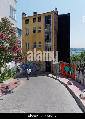 Pedestrian walks along a colourful street in Istanbul with a yellow building and an orange cat painted on a wall beside the pavement,Turkey Stock Photo