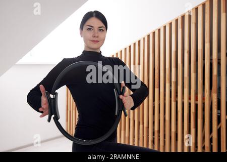 A young girl is engaged in Pilates in a bright studio. A slender brunette in a black bodysuit is doing exercises with a spring reformer. Healthy lifes Stock Photo