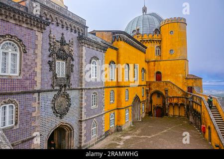 The brightly colored cylindric bastion in the New Palace at the Courtyard of Arches of the Pena Palace or Palácio da Pena historic palace castle in Sintra, Portugal. The fairytale castle palace is considered one of the finest examples of 19th century Portuguese Romanticism architecture in the world. Stock Photo