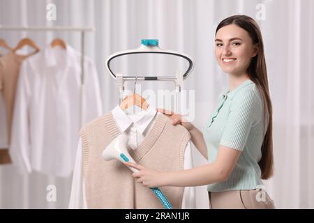 Woman steaming clothes on hanger at home, close up, handheld steamer in