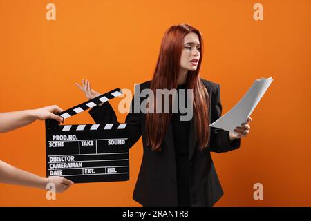 Actress performing role while second assistant camera holding clapperboard on orange background Stock Photo