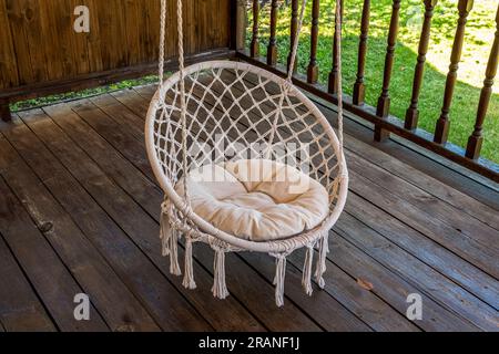 A white hammock chair hangs on the wooden deck of a private house. Stock Photo