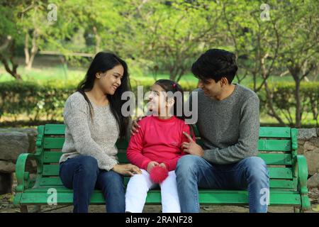Parents enjoying with daughter in park surrounded with greenery and serenity. They are having joyful and cheerful time together. Stock Photo
