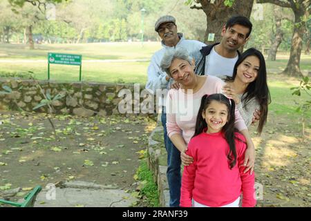 Grandparents enjoying with grand daughter in park, surrounded with greenery and serenity. They are having joyful and cheerful time together in greens. Stock Photo