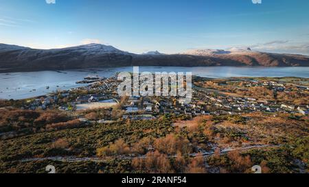 Aerial view of Ullapool on a sunny winter day, showcasing its snowy mountains and harbor Stock Photo