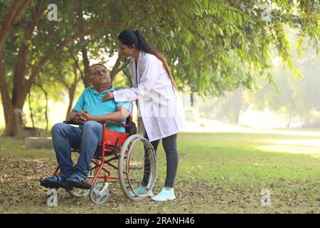 Doctor taking care of senior patient in hospital garden. The patient is disable of walking and getting treated by a specialist family doctor Stock Photo