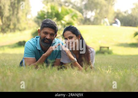 young couple dreaming for the property they are buying to purchase. Happy Indian couple lying on the grass waiting happily for their property Stock Photo