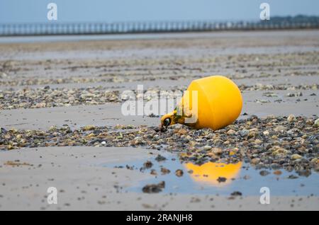 Float or buoy laying on sand on a beach at low tide, with a chain attached to something. Stock Photo