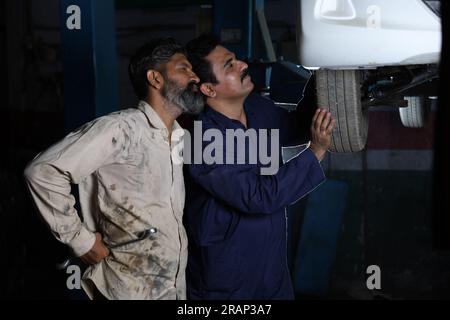 Car mechanics standing and working together in service station. Car specialists examining lifted car tyre. Professional repairmen talking, engaging Stock Photo