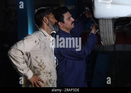 Car mechanics standing and working together in service station. Car specialists examining lifted car tyre. Professional repairmen talking, engaging Stock Photo