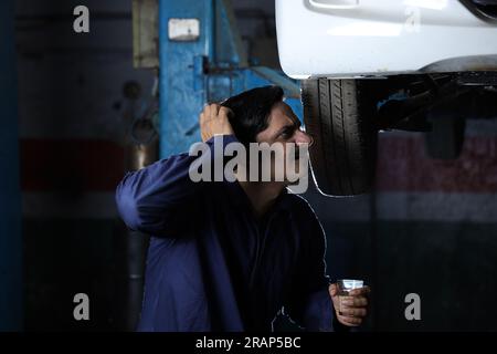 Portrait of happy car mechanic in moustache repairing and examining the lifted car. Car specialist is working on the tyre. Hard working Stock Photo