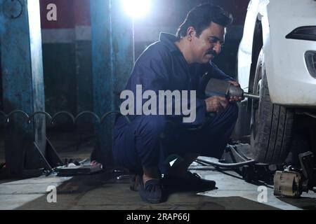 Portrait of happy car mechanic in moustache repairing and examining the lifted car. Car specialist is working on the tyre. Hard working Stock Photo