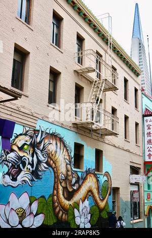 Mural with a Chinese dragon and lotus flowers on a building wall with the Transamerica Pyramid Chinatown Grant Avenue San Francisco California USA Stock Photo