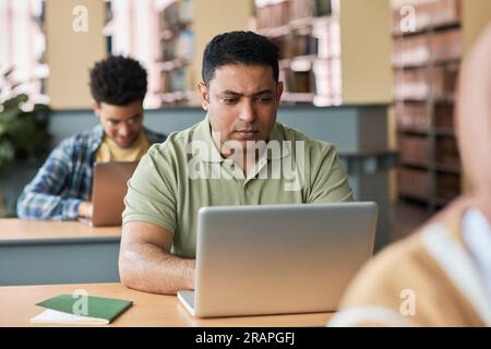 Adult student sitting at desk and using laptop at lesson with other students in class Stock Photo