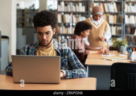 Adult student sitting in library and learning foreign language online using his laptop Stock Photo