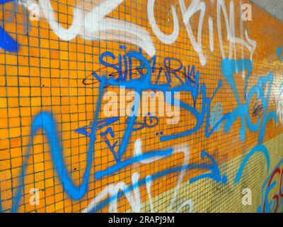 Orange ceramic tile wall vandalized with graffiti paintings. Close up shot, no people. Stock Photo