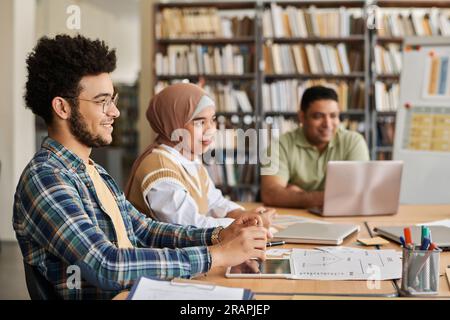 Migrant students studying foreign language while sitting together at table with computers and textbooks Stock Photo