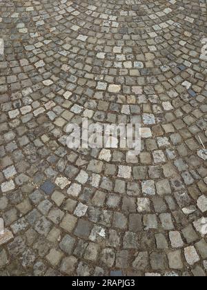Old rough cobblestone footpath pavement arranged in a circular radius. Top view, no people, Europe. Stock Photo