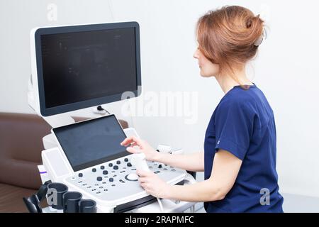Doctor woman in uniform sitting in office in hospital with ultrasound diagnostic machine equipment and ready to examine patients doing ultrasound of t Stock Photo