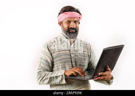 Portrait of an happy Indian bearded farmer man in rural India concept. White background cheerful confident farmer holding laptop and using technology. Stock Photo