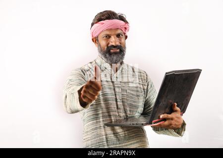 Portrait of an happy Indian bearded farmer man in rural India concept. White background cheerful confident farmer holding laptop and using technology. Stock Photo