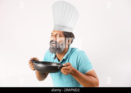 Portrait of Indian bearded chef man wearing t-shirt and chef cap. Happy smiling expressions white background. Holding spatula and frying spoon in hand Stock Photo