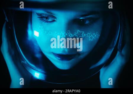A close-up portrait of a woman wearing an astronaut helmet with starry makeup against the backdrop of the dark cosmos. Space exploration and female em Stock Photo
