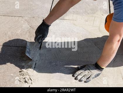 Real work scene, worker closes the empty spaces between the bricks of a pedestrian roadway with mortar. Stock Photo
